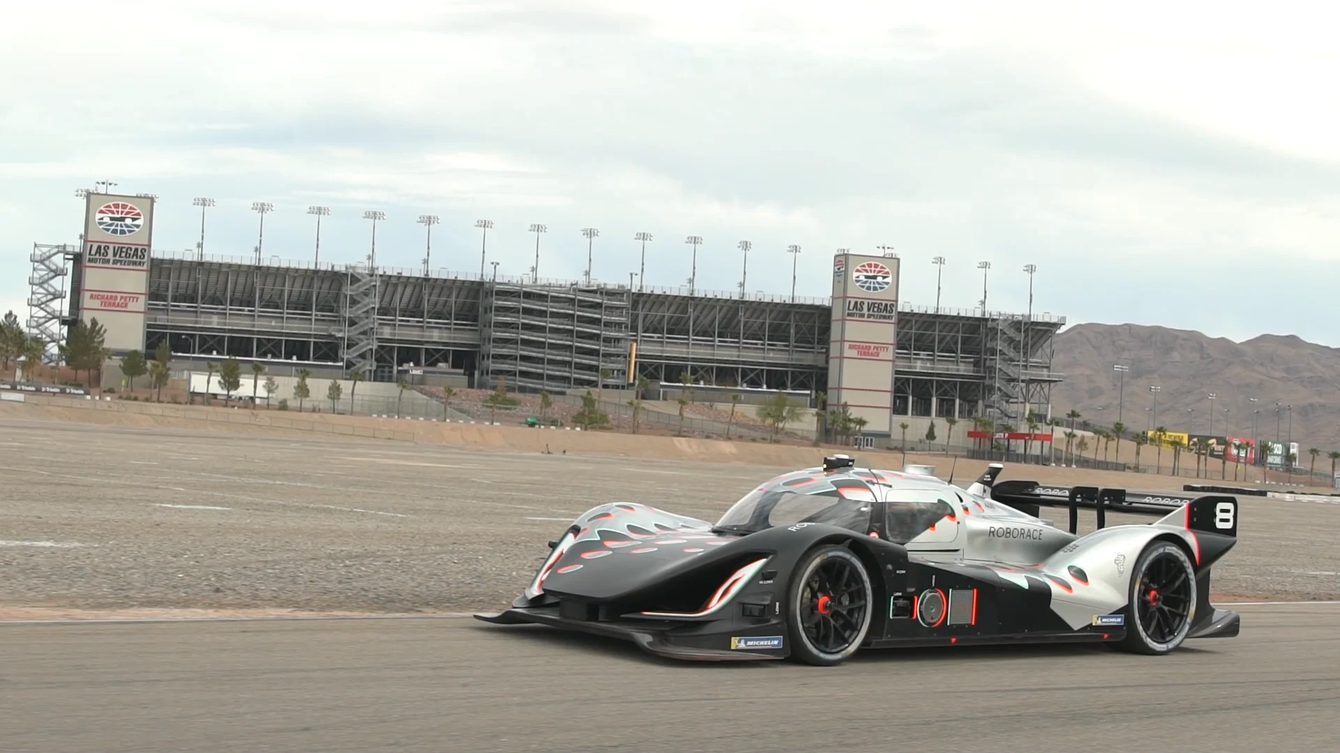 A black, silver, and red Roborace car driving on the circuit at Las Vegas Motor Speedway.